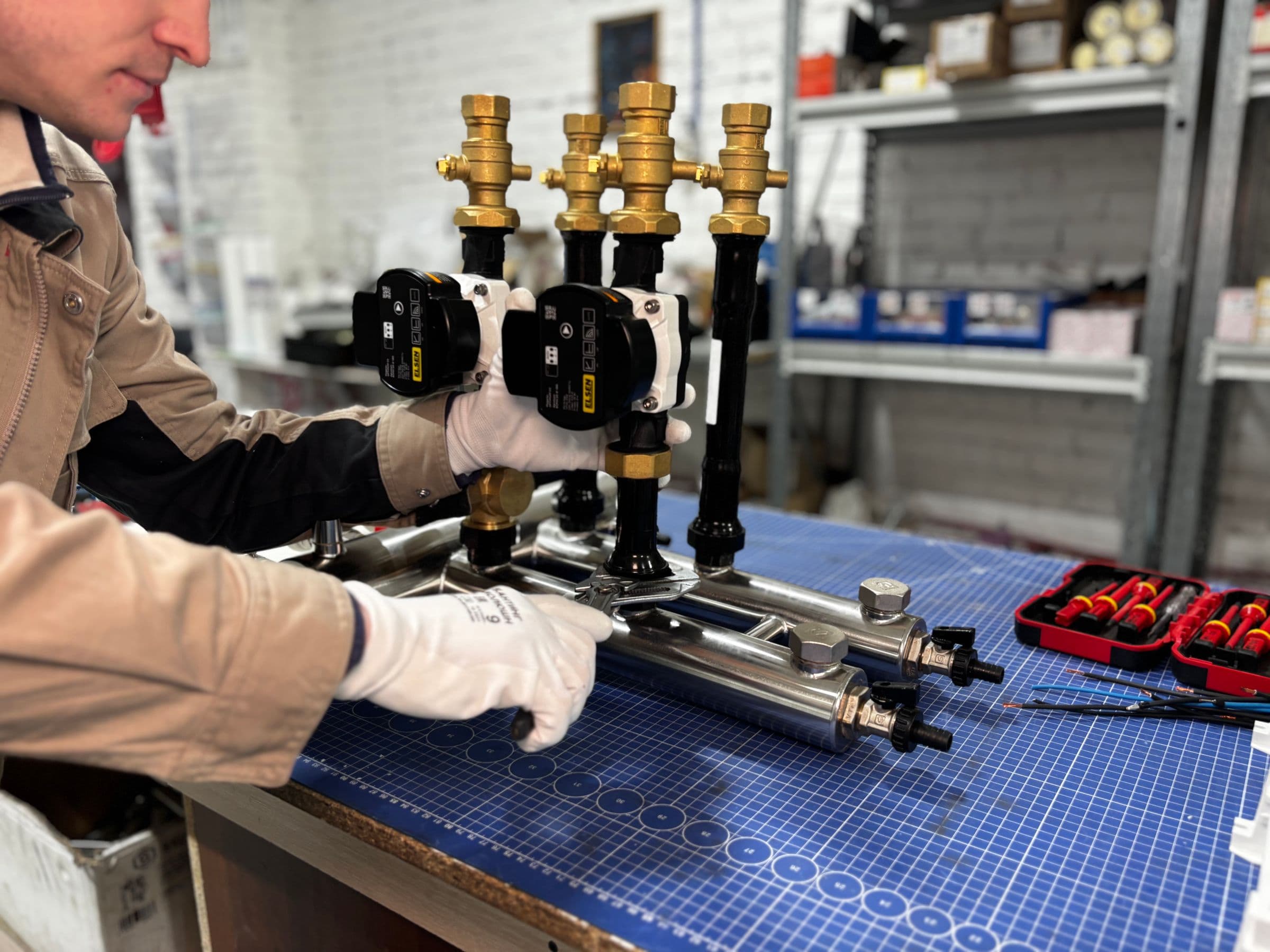 Monteur baut einen Heizungsverteiler mit Pumpen und Ventilen zusammen